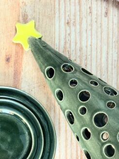 Ażurowa choinka ceramiczna 17 cm stojąca na drewnianym blacie z drobnymi bombkami w tle