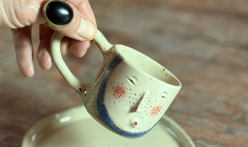 Rękodzieło z nakrapianej gliny – filiżanka z twarzą i talerzyk o organicznym kształcie.